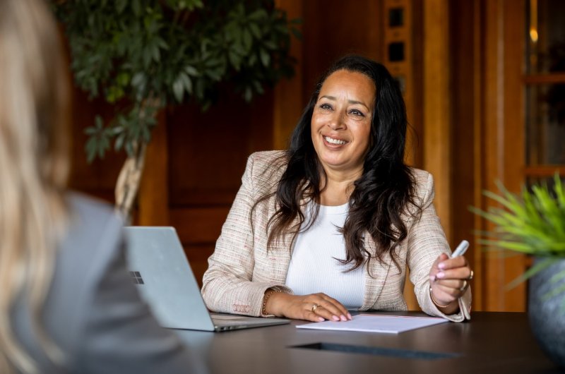 Twee vrouwen in gesprek aan een tafel. De een is financieel adviseur van Ooms Financieel Advies, de ander is een klant.
